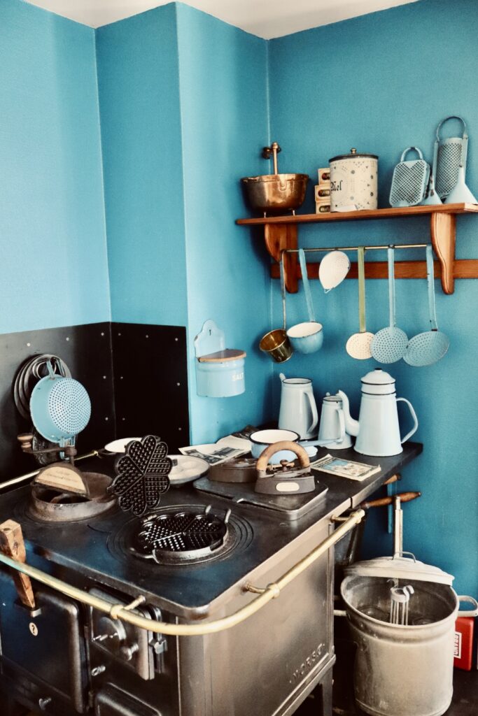 alter Küchenherd mit Töpfen etc. vor blauer Wand